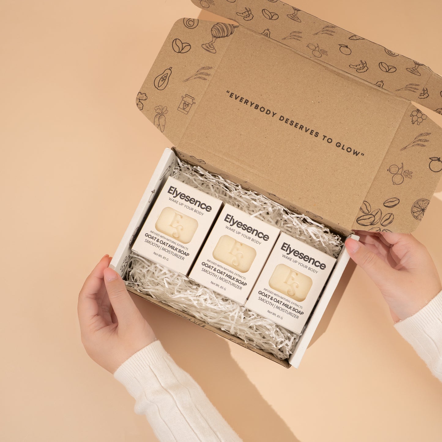 Three Elyesence Goat & Oat Milk Soap bars in an open kraft gift box with shredded filler, labeled 'Everybody Deserves to Glow