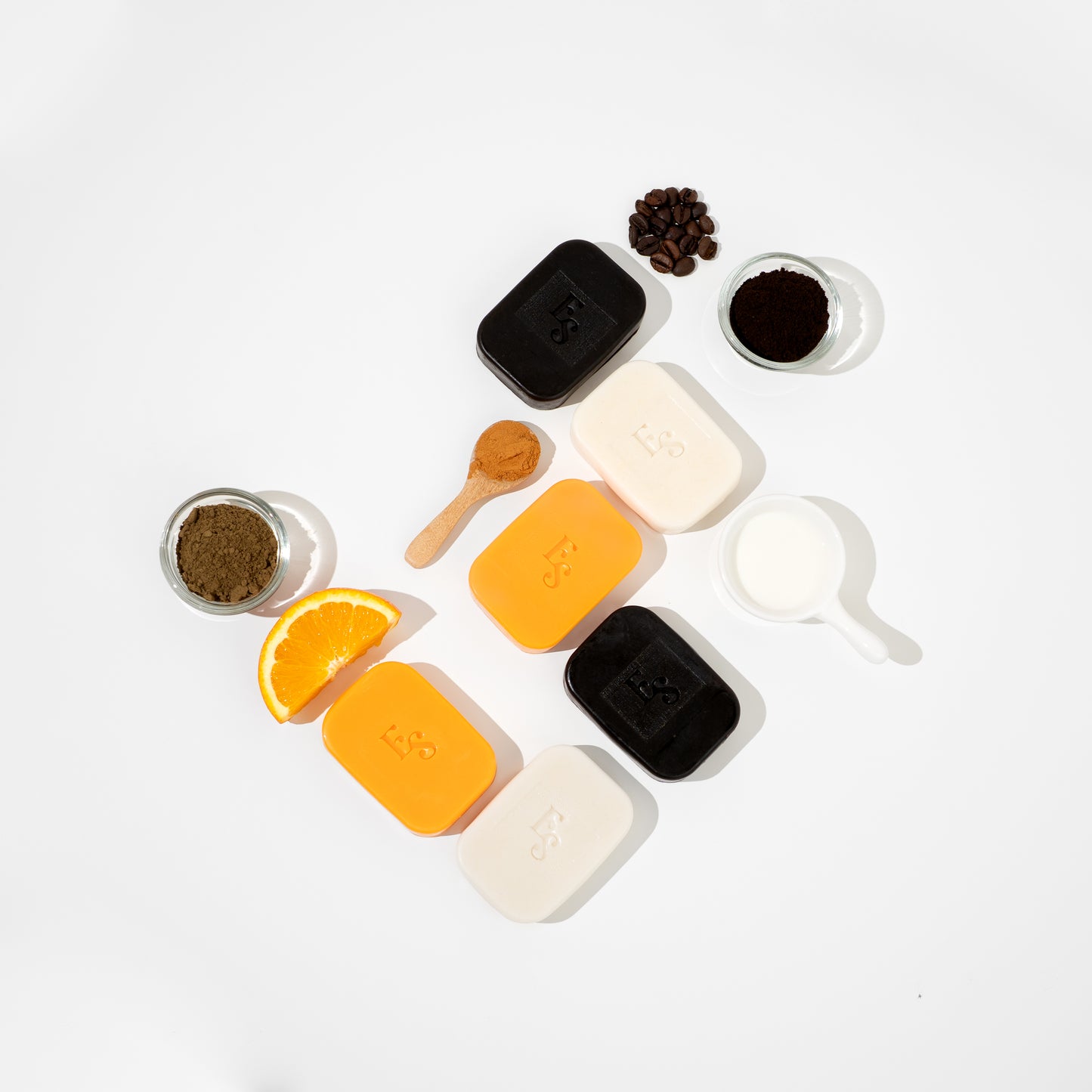 Flat lay of all Elyesence soaps: coffee, orange, and goat milk with natural ingredients on white background