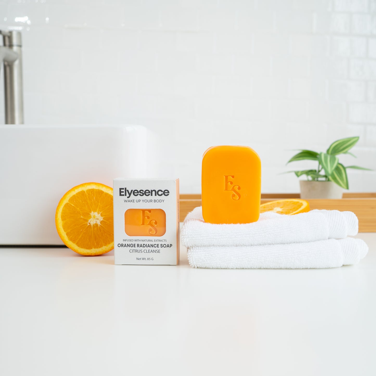 Elyesence Orange Radiance Soap bar with box, white towel, and fresh orange slices in a modern bathroom setup