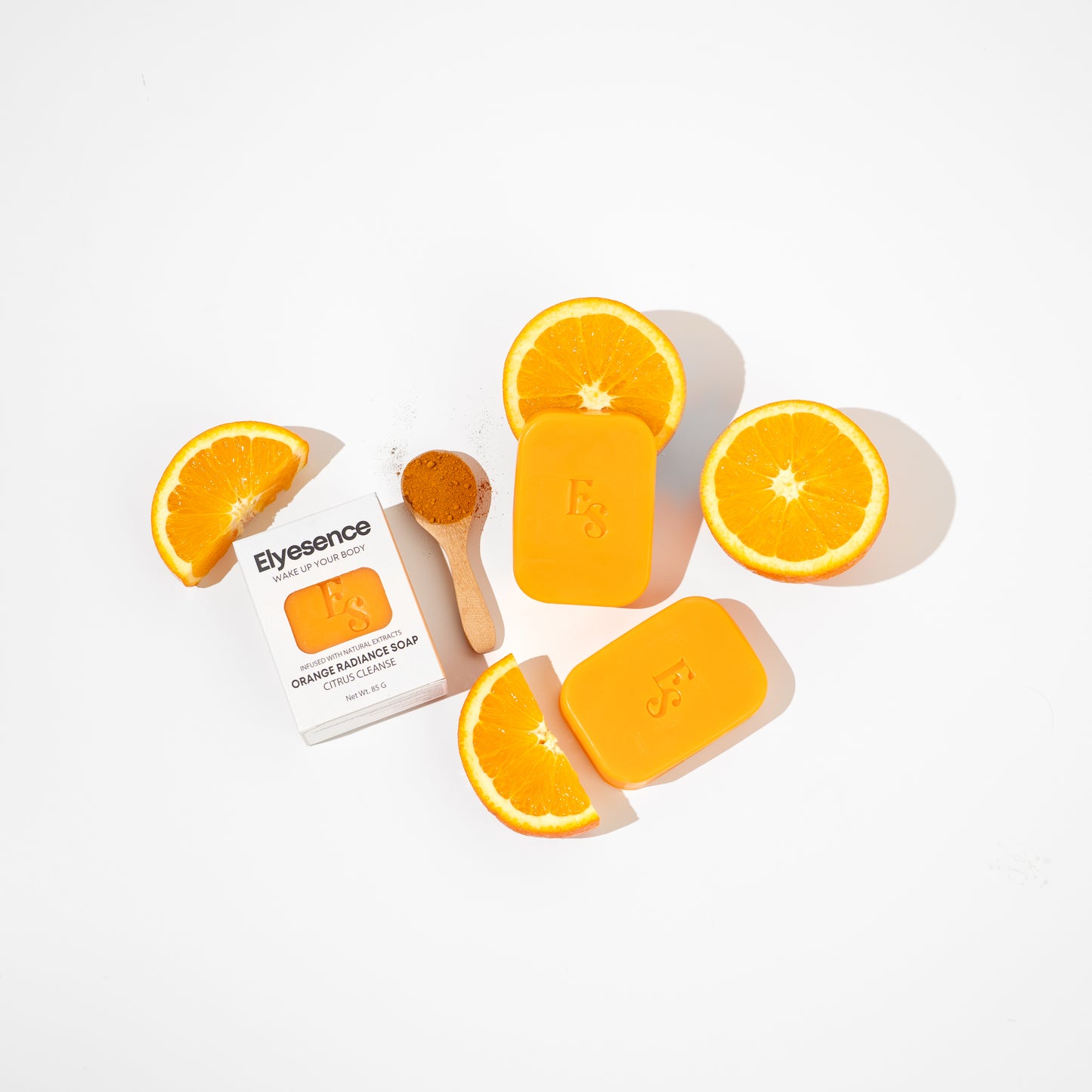 Three Orange Radiance Soap bars from Elyesence with turmeric, orange slices, and product box in a bright white background