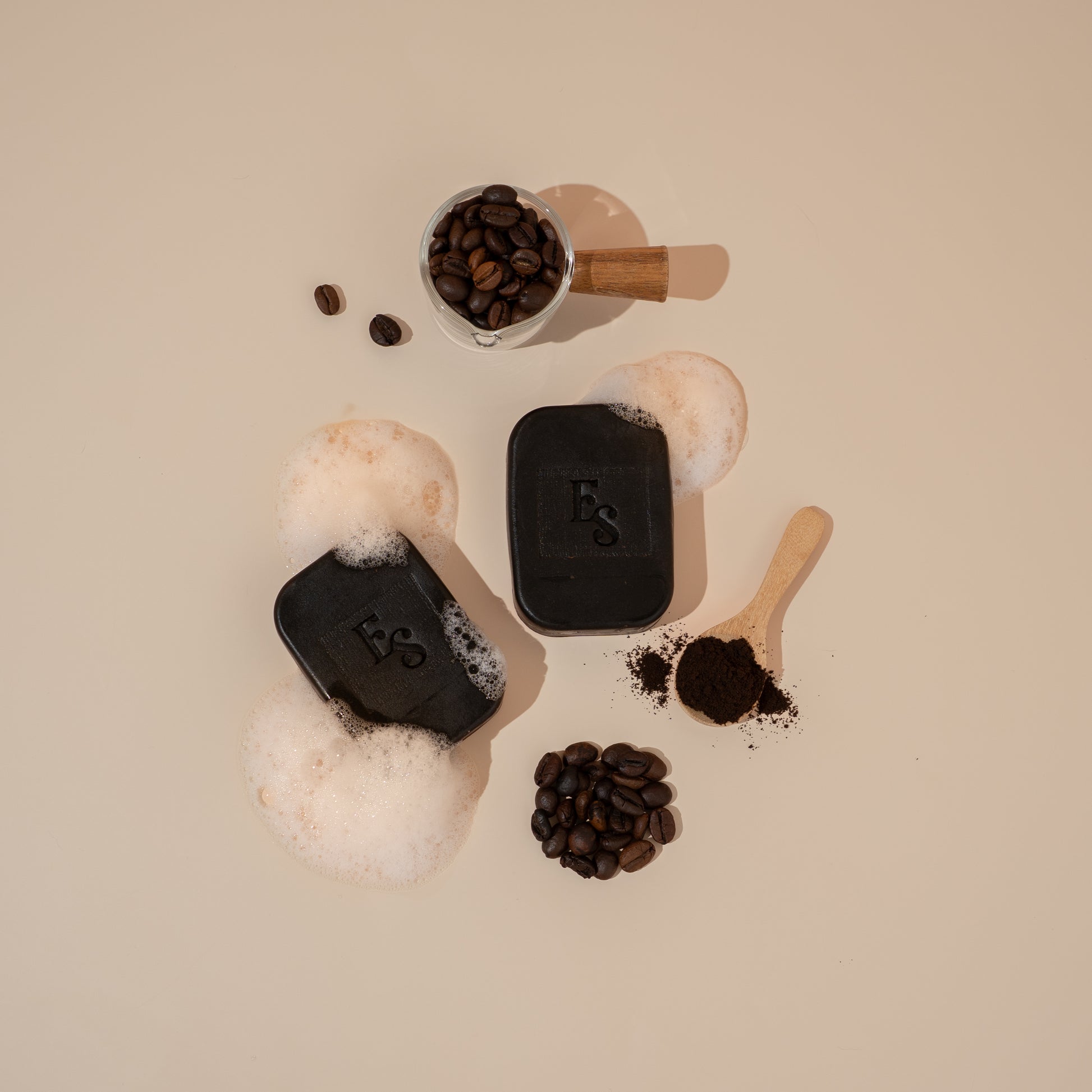Flatlay of Elyesence Arabica Coffee Soap bars with scattered coffee beans and exfoliating grounds.